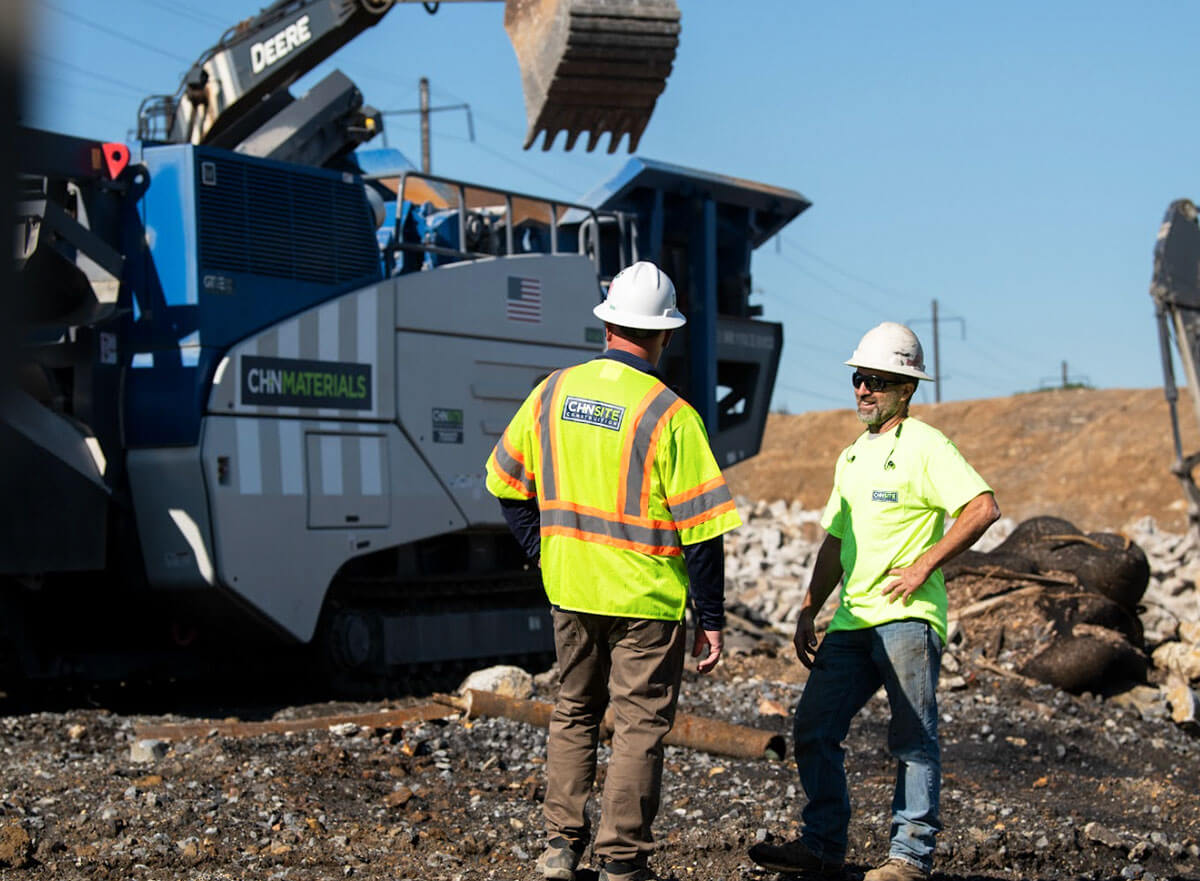 Two CH+N team members on a construction site with an excavator and CH+N Materials truck